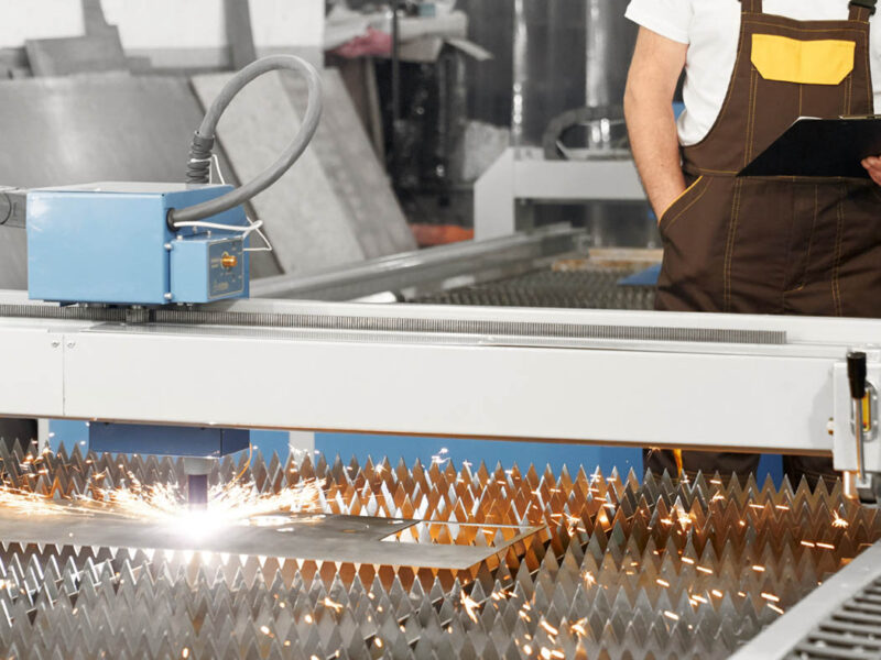 Engineer observing plasma laser cutting metal sheet.